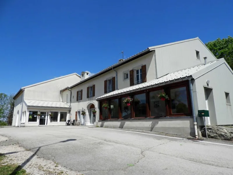 Façade en pierre de la Ferme Léonie sous ciel bleu, volets bois et véranda vitrée à l'entrée