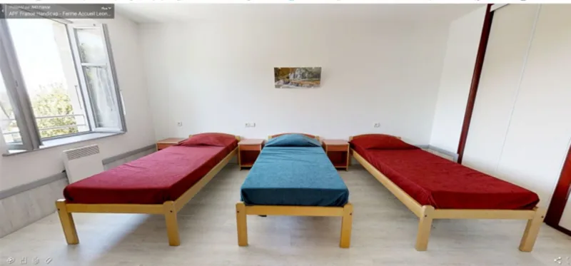 Chambre dortoir avec trois lits simples aux couvre-lits rouge et bleu, fenêtre lumineuse