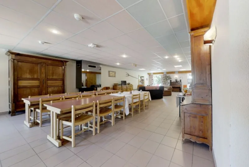 Grande salle à manger avec longues tables en bois et armoire ancienne pour les repas de groupe
