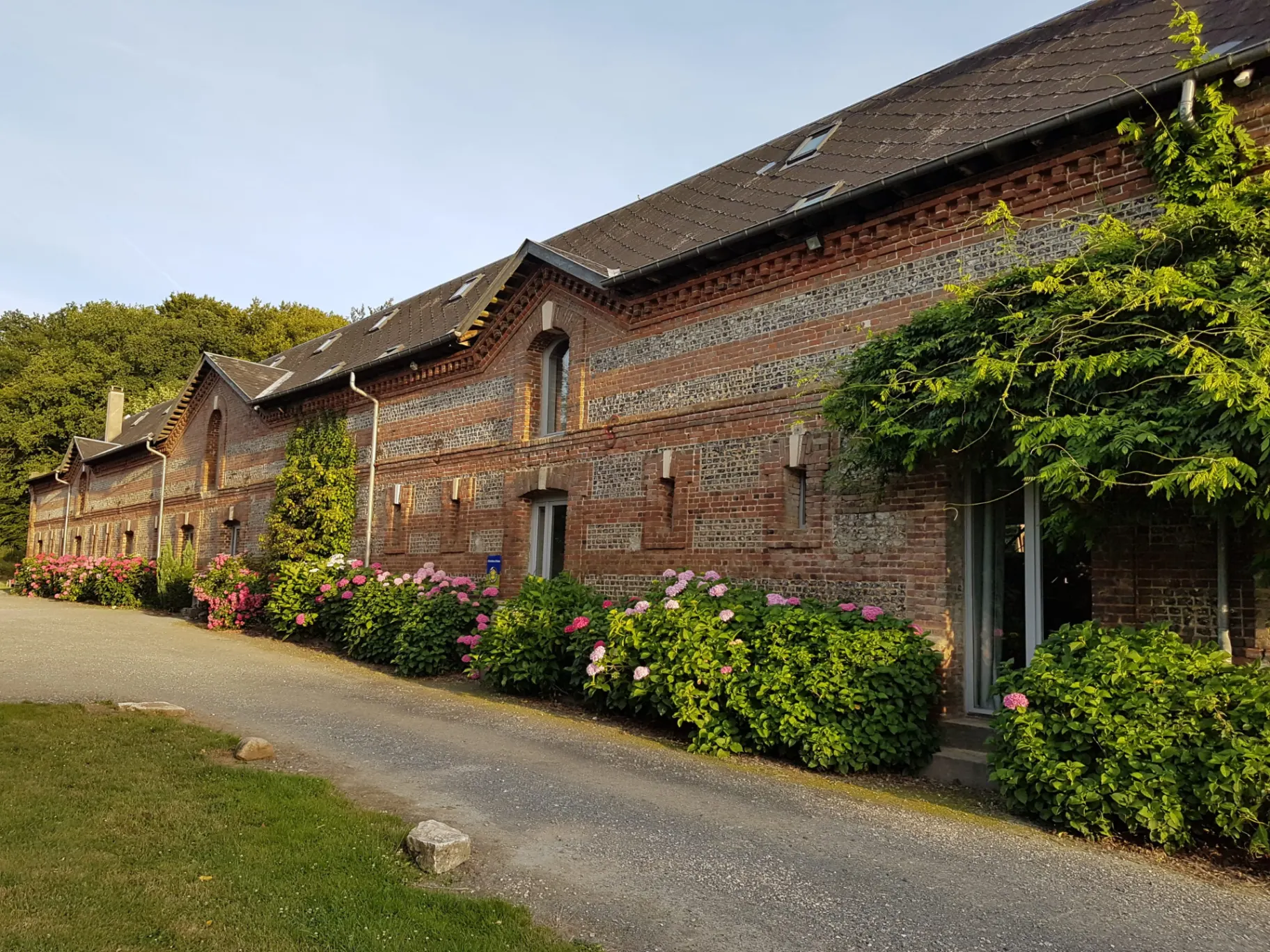 Gîte de groupe Le Clos de la Beauce à Clères — Façade en briques et silex du Clos de la Beauce, longère normande du XVIIIe siècle fleurie d'hortensias, capacité 40 personnes