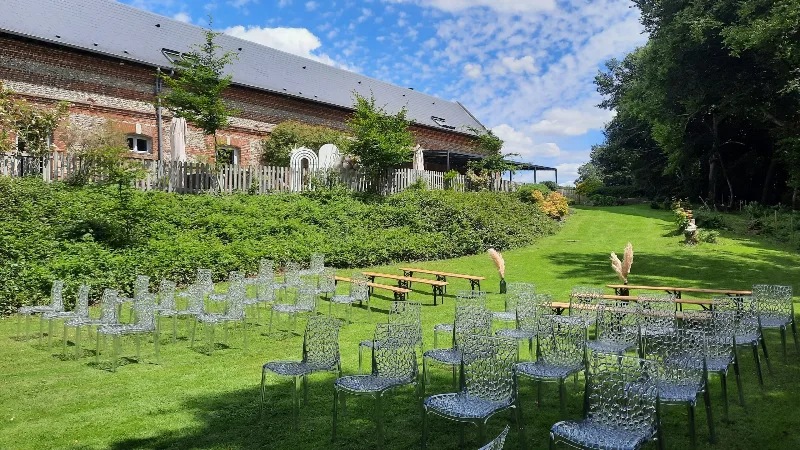 Jardin arboré avec chaises de cérémonie installées sur la pelouse face à la longère