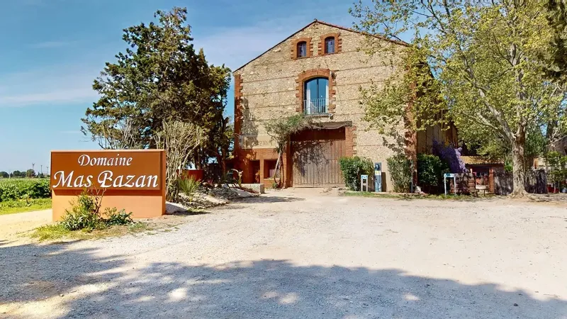 Façade en pierre catalane du Domaine Mas Bazan avec grand portail en bois et enseigne à l'entrée