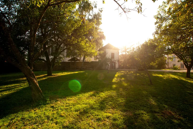 Verger arboré du domaine au coucher du soleil, avec vue sur les bâtiments du château-ferme