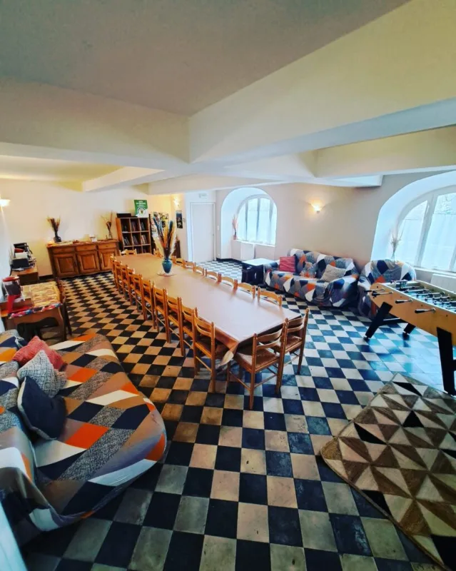 Grande salle de vie conviviale avec longue tablée, canapés et baby-foot