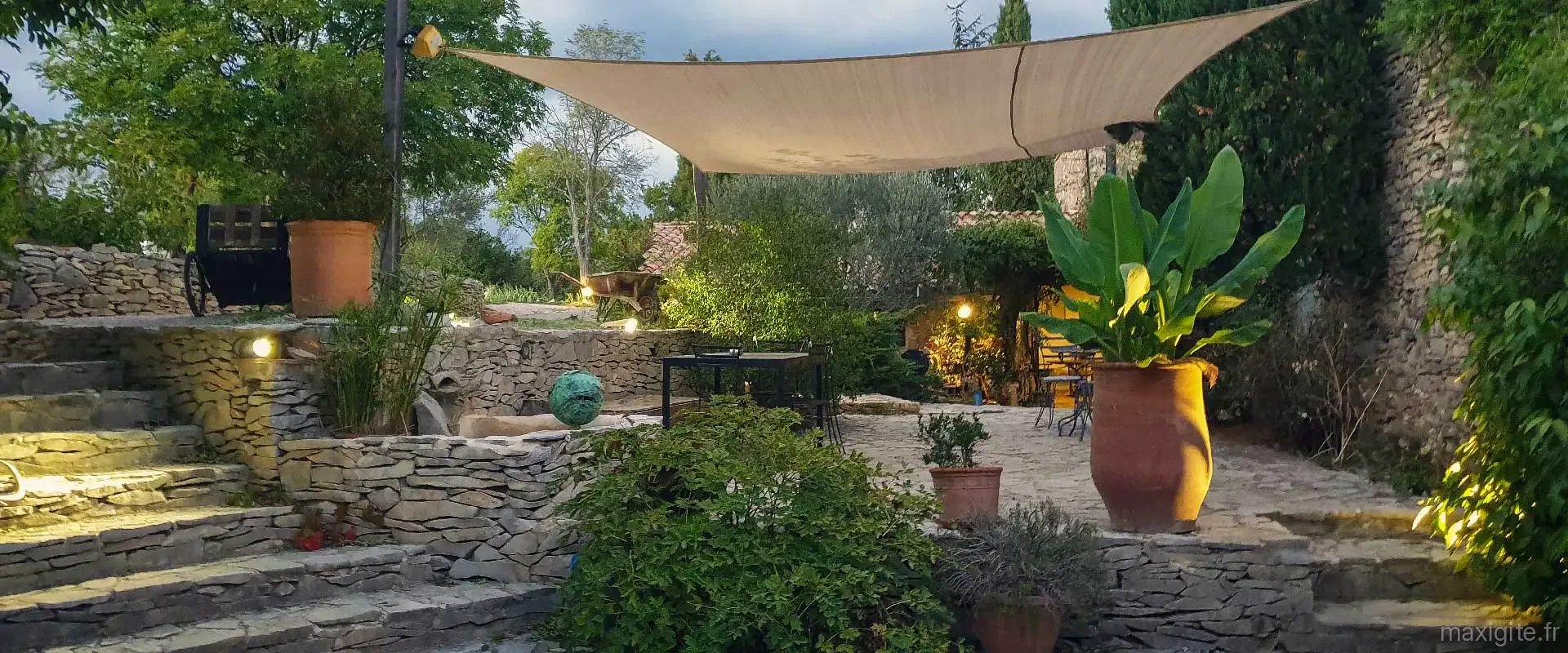 Terrasse en pierre éclairée avec voile d'ombrage et mobilier de jardin