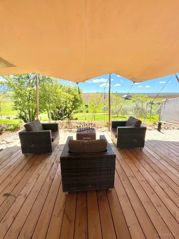 Coin salon extérieur couvert avec canapés en rotin et vue sur la campagne