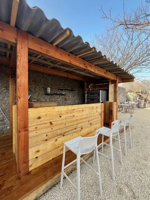 Bar extérieur en bois avec tabourets, ouvert sur la terrasse du domaine