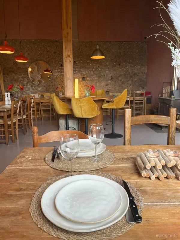 Salle de restaurant chaleureuse avec table dressée, murs en pierre et poutres apparentes