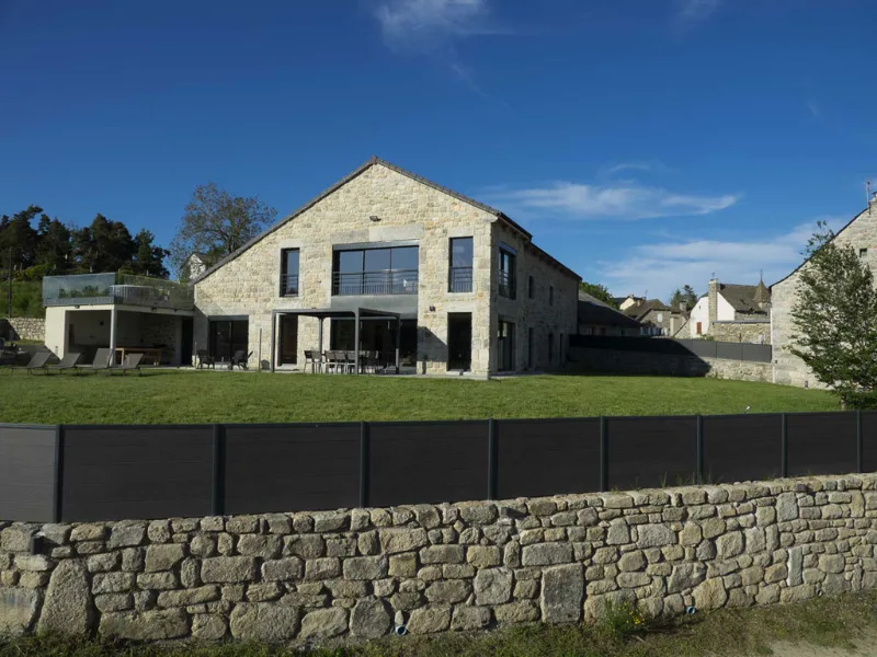 Grande bâtisse en pierre au toit à double pente, terrasse et jardin arboré en Aubrac