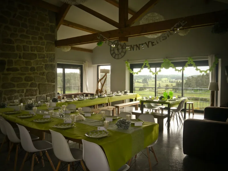Grande salle commune sous charpente en bois, tables dressées et baies vitrées sur la campagne