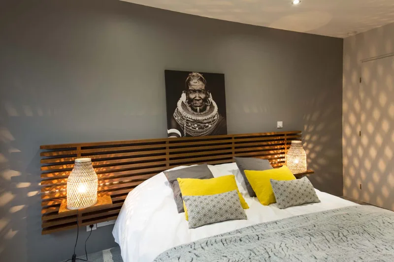 Chambre double aux tons gris avec tête de lit en bois clair et coussins jaunes