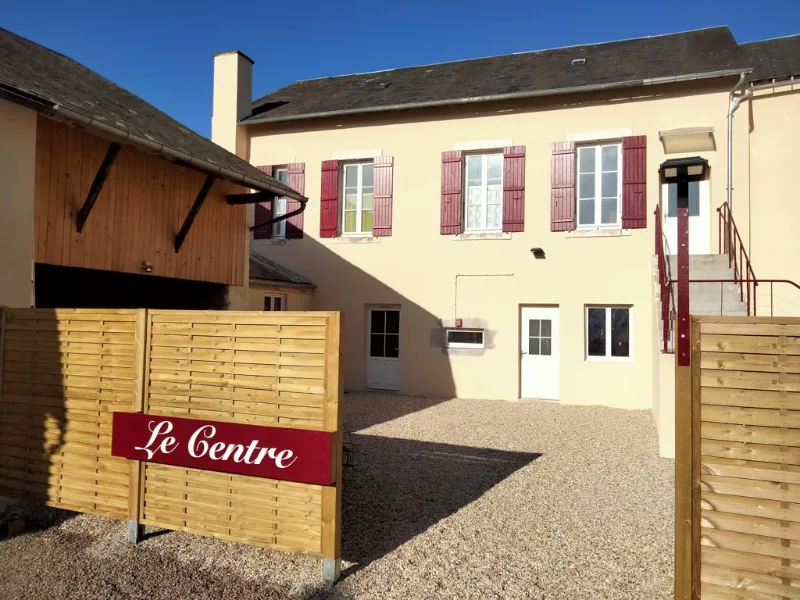 Façade du bâtiment en pierre avec volets rouges et enseigne Le Centre