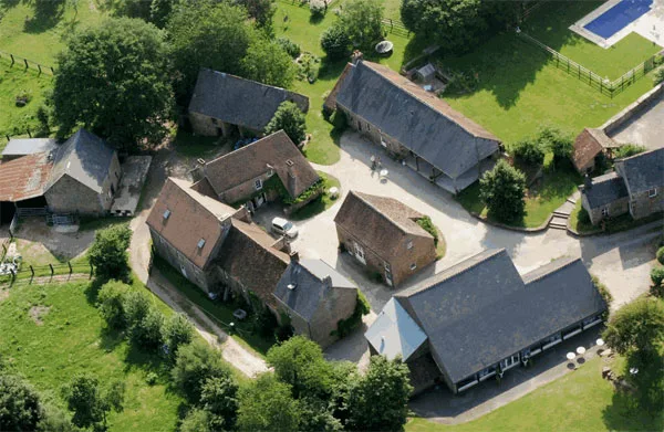 Gîte de groupe Le Hameau de la Fouquière à Joué-du-Bois — Vue aérienne du hameau avec plusieurs bâtiments en pierre autour d'une cour et jardins arborés, capacité 82 personnes