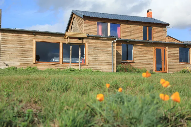 Façade en bois moderne de la maison principale avec grande baie vitrée et toit en zinc