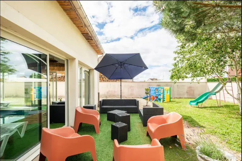 Terrasse extérieure couverte avec salon de jardin, vue sur la pelouse et les jeux d'enfants