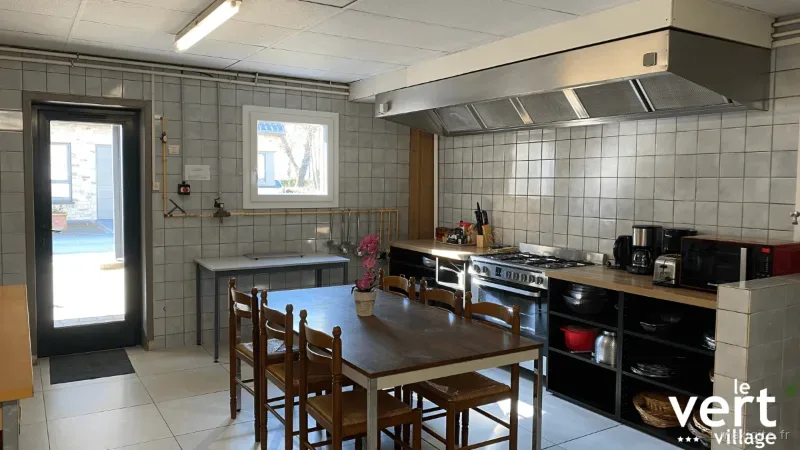 Cuisine collective équipée avec grande table en bois, cuisinière et hotte professionnelle