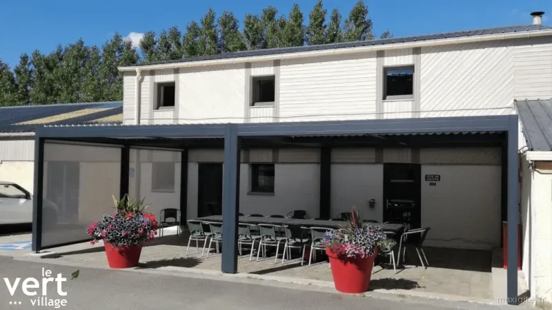 Façade du Vert Village avec terrasse couverte, tables et pergola pour le gîte de groupe