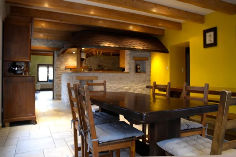 Salle à manger conviviale avec grande table en bois sous une hotte en pierre traditionnelle