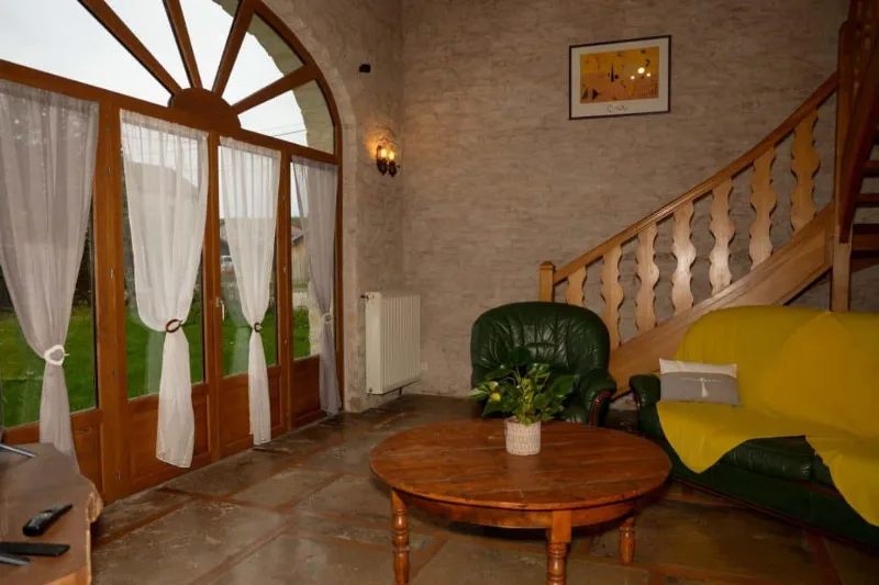 Salon avec cheminée en pierre, canapés en cuir et escalier en bois menant à l'étage
