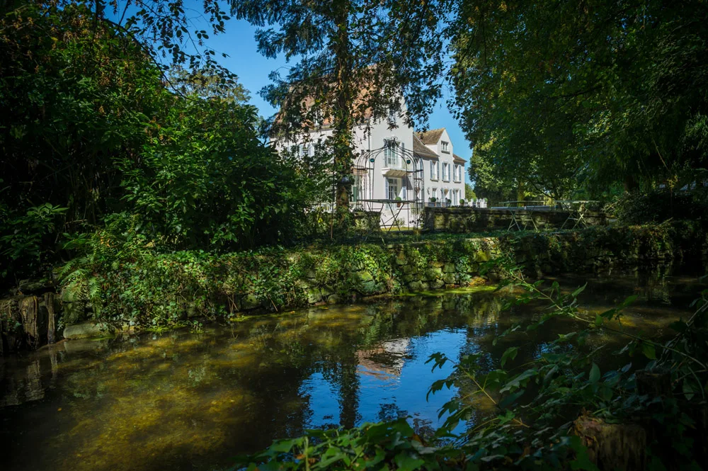 Gîte de groupe Domaine du Moulin des Noues à Soisy-sur-École — Façade du domaine en pierre au bord de la rivière, entourée d'arbres centenaires, capacité 22 personnes