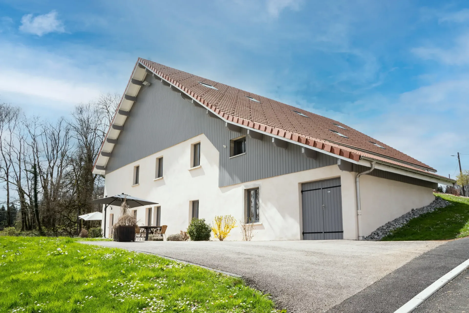 Gîte de groupe Les Gîtes du Sapey à Les Premiers Sapins — Façade en bardage gris et enduit blanc du grand chalet, sous un ciel bleu dégagé, capacité 15 personnes