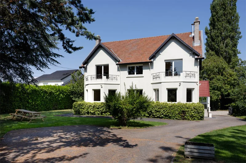 Façade en pierre blanche de la villa avec toiture à deux pans et jardin arboré
