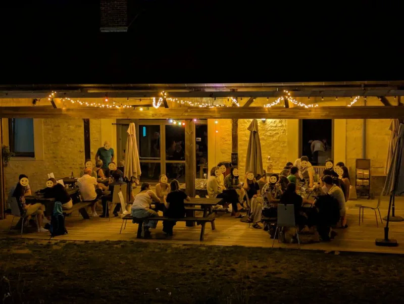 Terrasse couverte illuminée en soirée avec grandes tablées conviviales