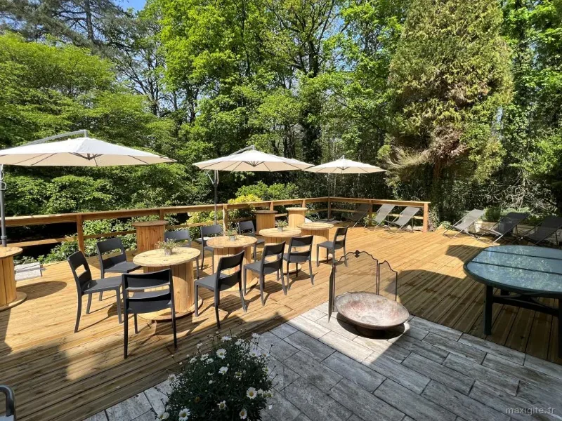 Terrasse en bois avec tables rondes, chaises et parasols au milieu des arbres