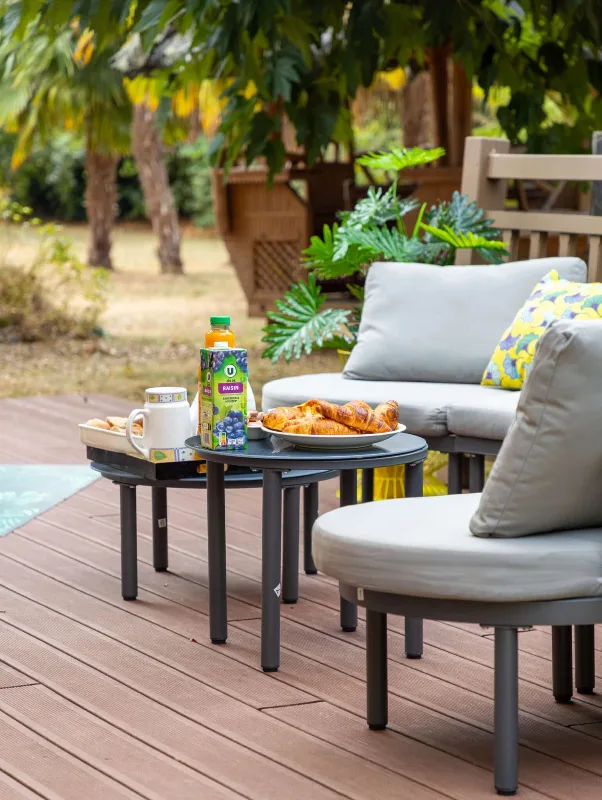 Terrasse en bois avec salon extérieur, coussins et petit-déjeuner servi en plein air