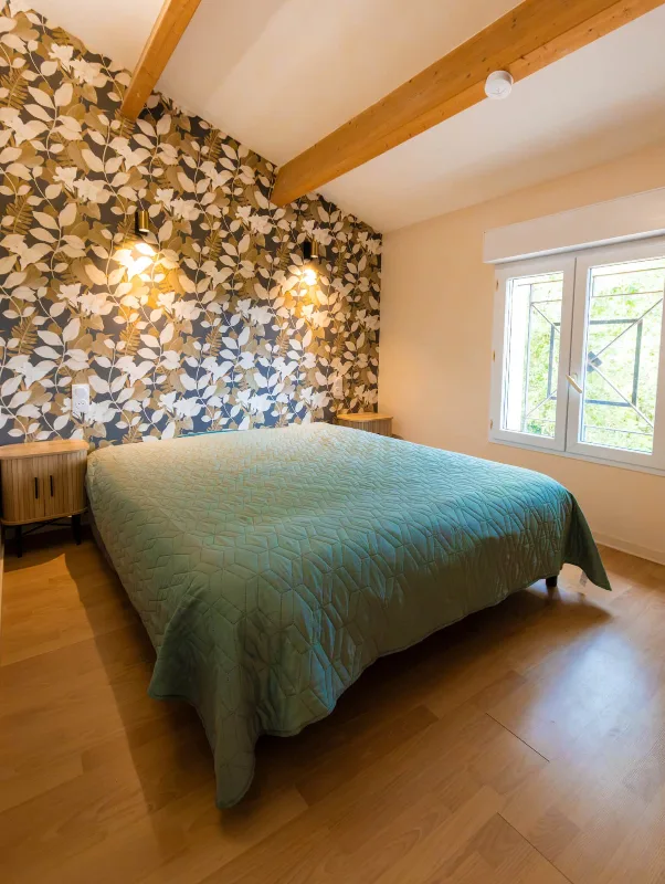Chambre lumineuse avec grand lit, tête de lit à motifs floraux et poutres apparentes