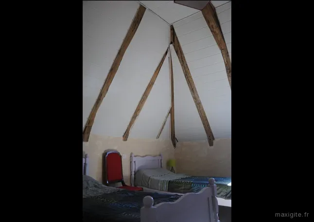 Chambre mansardée avec deux lits simples sous la charpente en bois