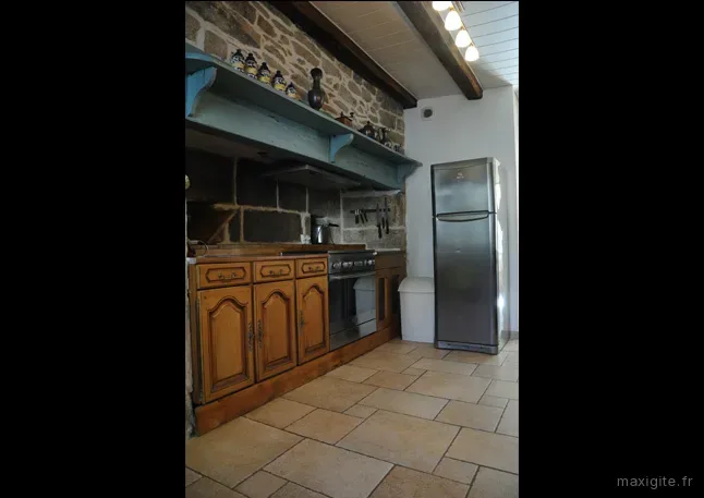 Cuisine campagnarde avec étagère bleue sur mur en pierre et réfrigérateur inox