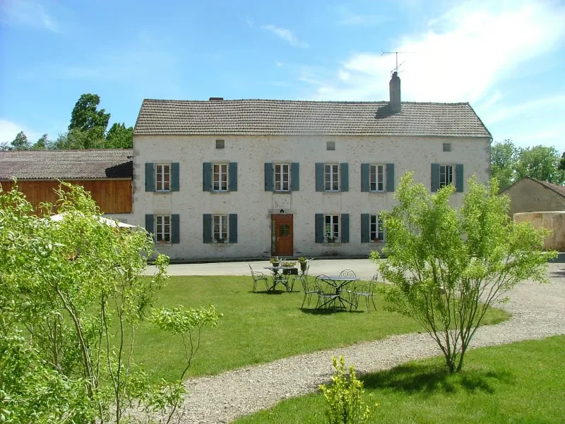 Façade principale de la ferme en pierre avec volets bleus et grand jardin