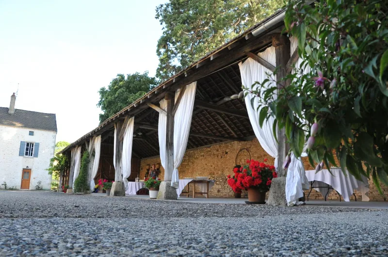 Grange ouverte aménagée en espace de réception avec rideaux blancs et tables dressées