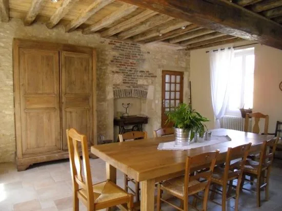 Grande salle à manger avec poutres apparentes, cheminée en pierre et table en bois pour groupe