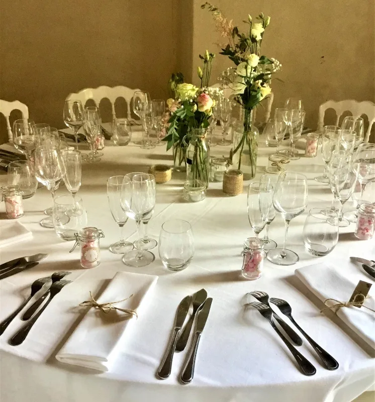 Table ronde dressée pour un repas de groupe avec vaisselle et compositions florales