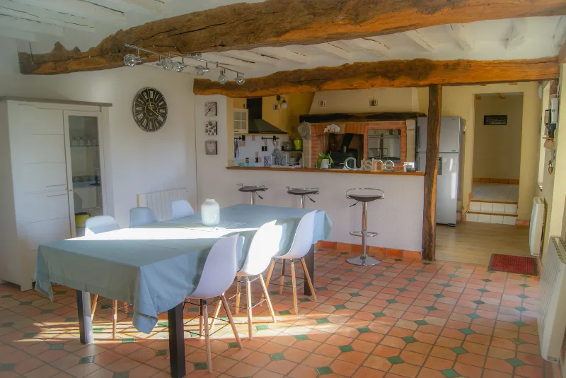 Cuisine ouverte sur salle à manger avec grande table, poutres apparentes et bar