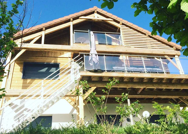 Gîte de groupe Chalet Lucy - Chalets Les Biches à Gérardmer — Façade en bois du Chalet Lucy avec grand balcon, terrasse et escalier extérieur, capacité 14 personnes
