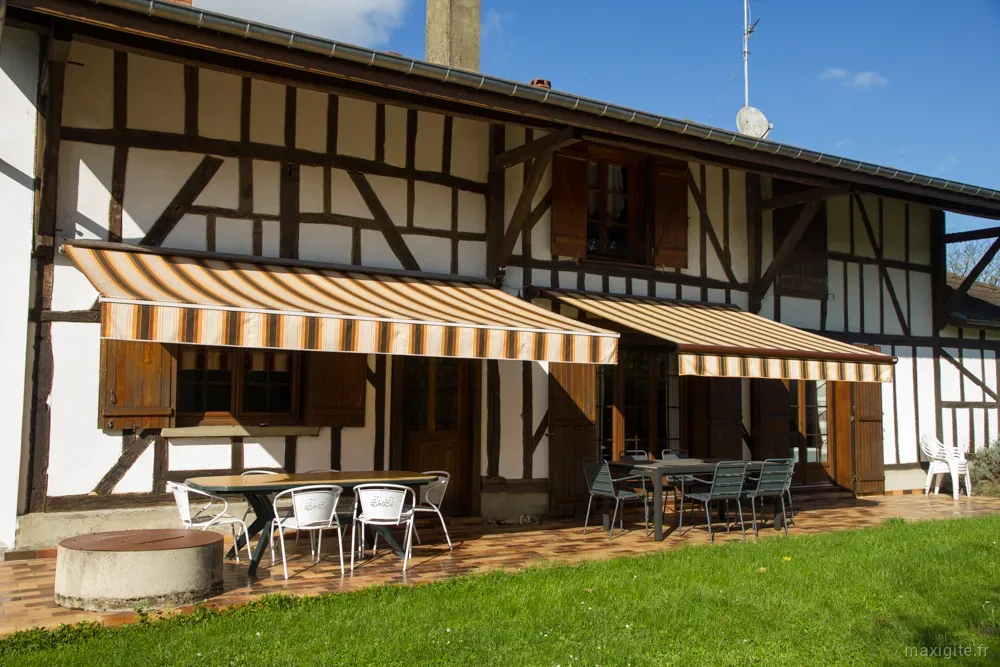 Gîte de groupe Gîte des 3 sillons à Rives-Dervoises — Façade à pans de bois du gîte avec terrasse couverte, tonnelle et mobilier de jardin, capacité 12 personnes