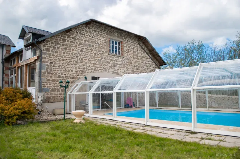 Piscine intérieure couverte avec structure vitrée, transats et vue sur le mur en pierre