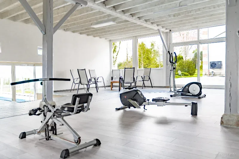 Salle de sport avec vélo elliptique, rameur et appareil de fitness, grandes baies vitrées