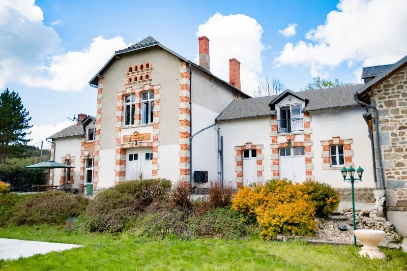 Façade du château avec briques et pierres orangées, jardin arboré et parterres fleuris