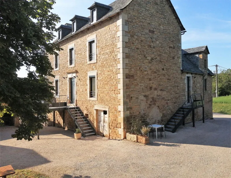 Façade en pierre du gîte avec escaliers extérieurs et terrasse ombragée par un arbre