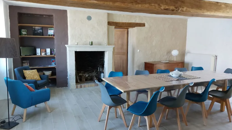 Salle à manger avec grande table en bois, cheminée en pierre et bibliothèque