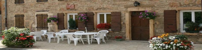 Façade en pierres dorées du gîte avec terrasse fleurie et salon de jardin