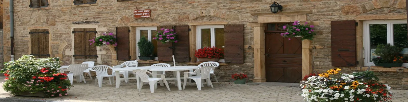 Gîte de groupe Gîte des Pierres Dorées à Rivolet — Façade en pierres dorées du gîte avec terrasse fleurie et salon de jardin, capacité 25 personnes