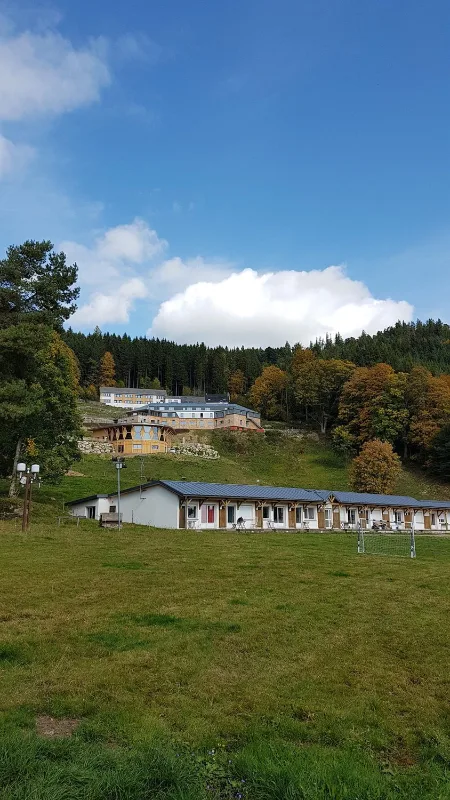 Vue d'ensemble du domaine sur un coteau boisé, avec grand pré et bâtiments en pierre et bois