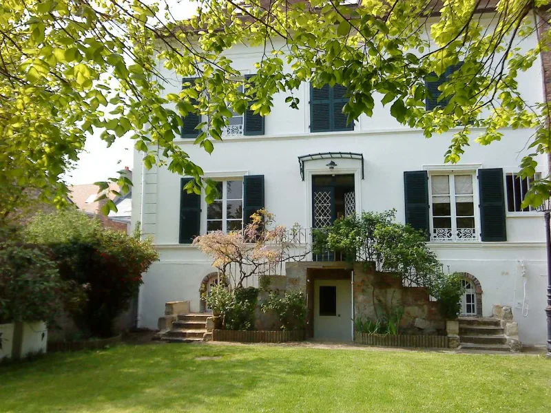 Façade blanche de la villa avec jardin arboré et perron en pierre