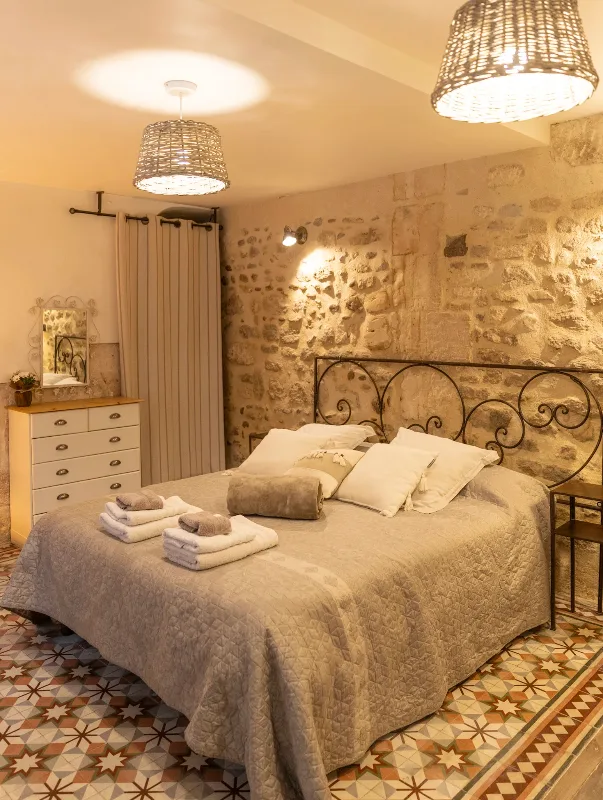 Chambre avec tête de lit en fer forgé et mur en pierre apparente