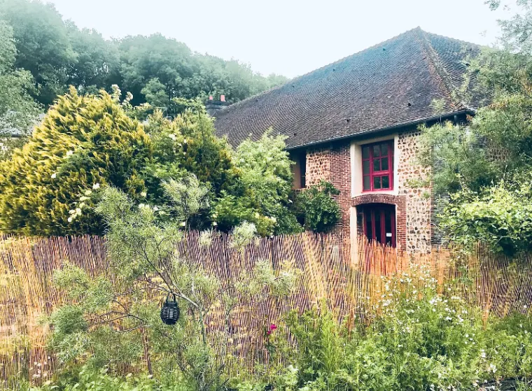 Façade en pierre et brique du bâtiment du XVIIe siècle avec fenêtres à cadre rouge, entourée d'un jardin verdoyant